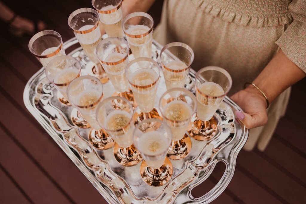 From above of crop female holding tray with glasses of champagne in daylight